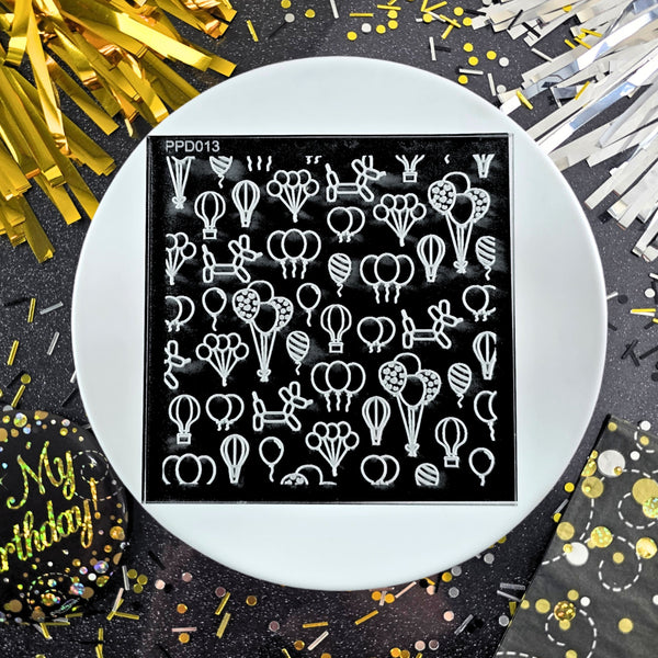 Stamping plate with balloon design on a black background, surrounded by confetti and party decorations.