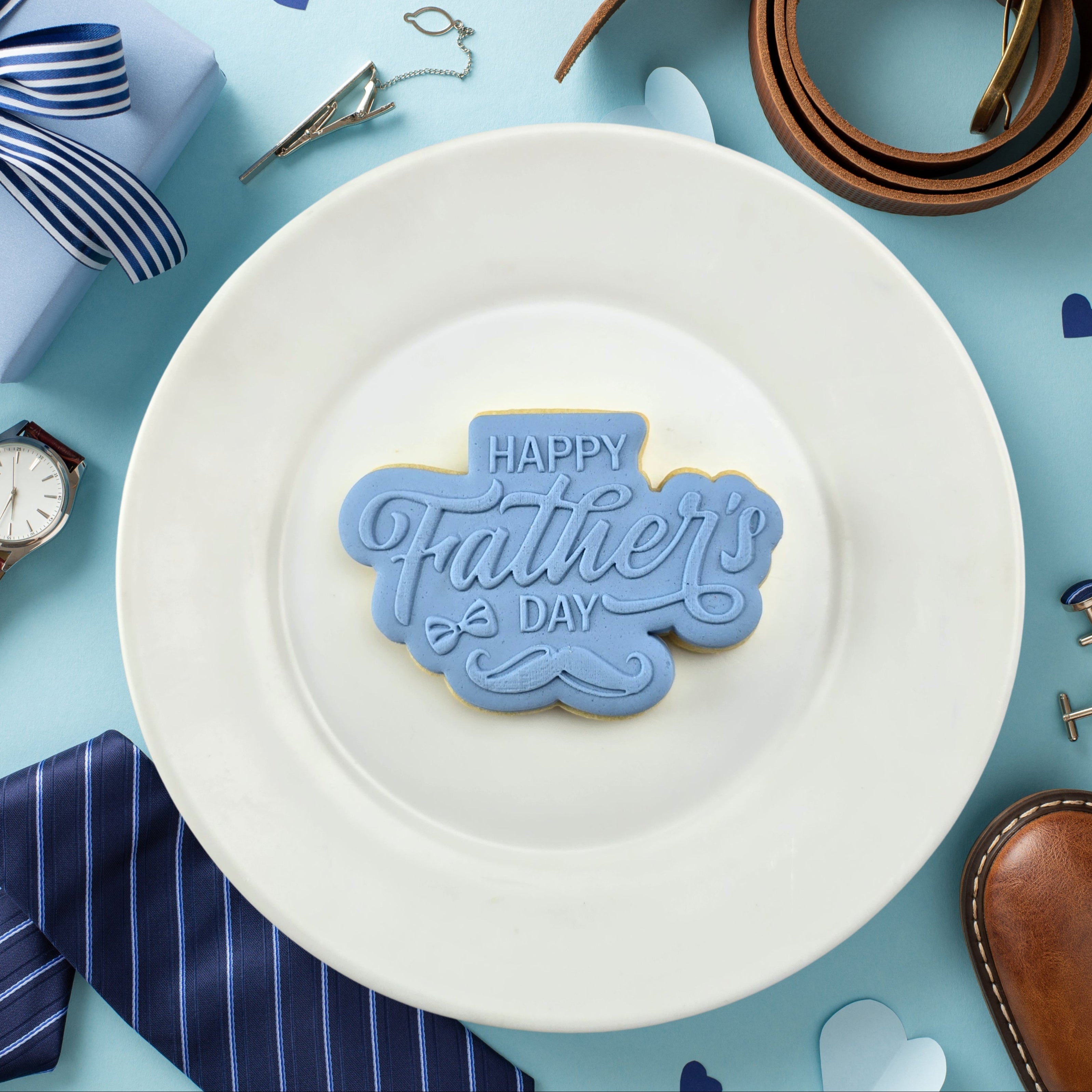 White plate with a 'Happy Father's Day' cookie on a blue background with Father's Day-themed items.