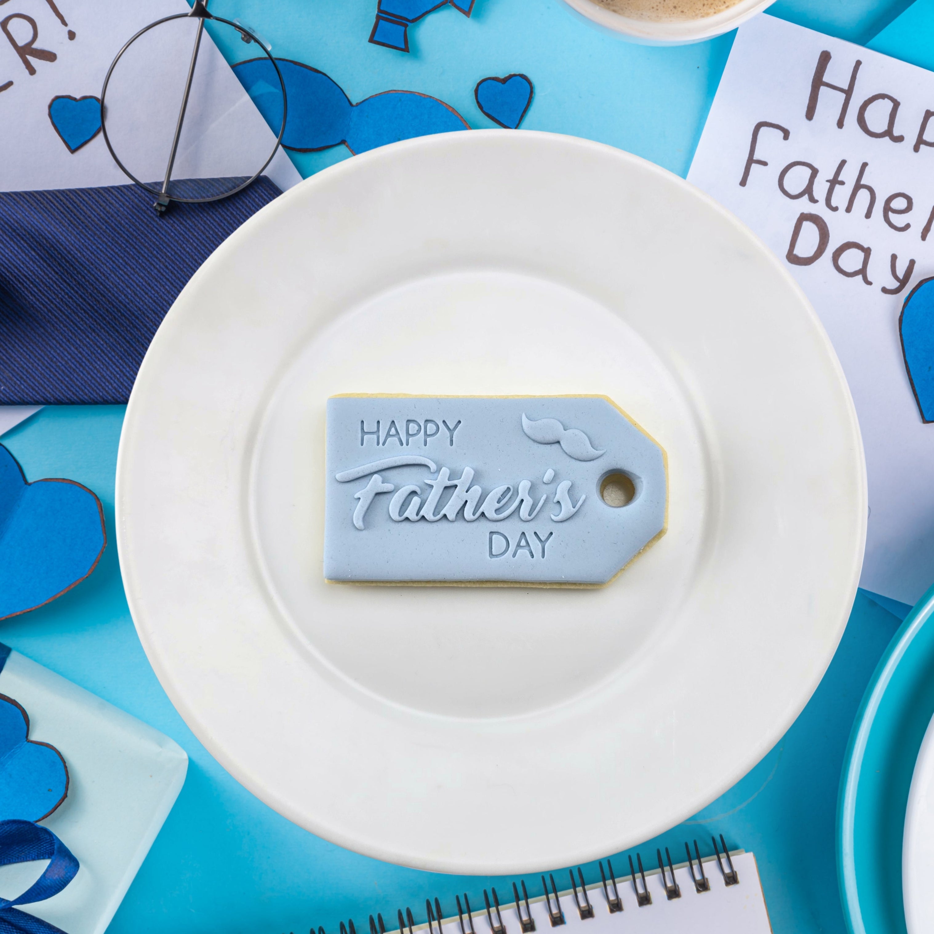 White plate with a 'Happy Father's Day' tag on a blue background with Father's Day cards and decorations.