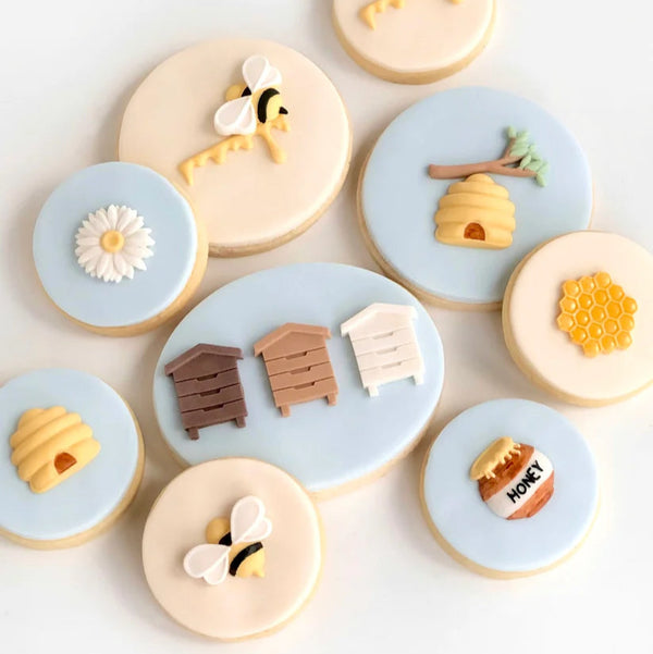 Decorative cookies with bee, honeycomb, and beehive designs on a light background