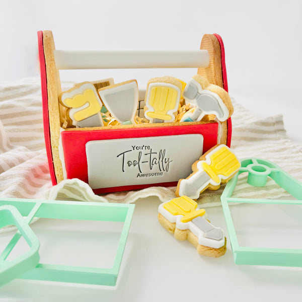 Decorative cookie set shaped like tools in a red toolbox with 'You're Tool-tally Awesome' text on a white background.